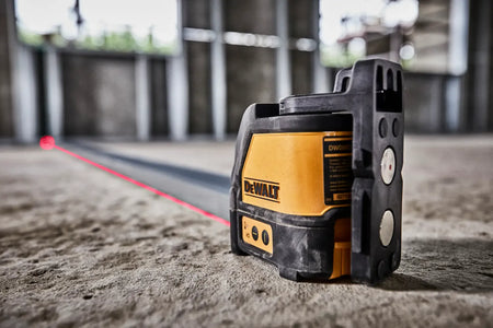 A perspective view of the DW088K laser unit in operation on a construction site. The shot emphasizes the rugged over-molding and the magnetic pivot bracket as the unit projects a long, bright red laser line across a concrete floor for floor-to-ceiling alignment.