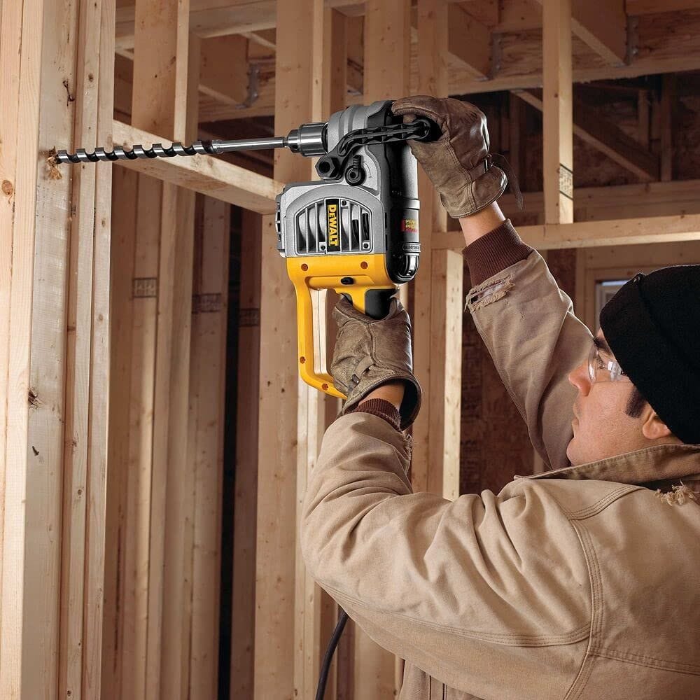 A lifestyle image of a tradesman using a heavy-duty DEWALT D-handle drill to drive the DW1686 power ship auger bit into a residential wall stud. The image demonstrates the tool's effectiveness for running large electrical or plumbing lines through structural framing.