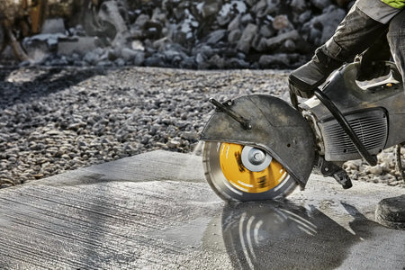 A wide action shot of a professional contractor using a DEWALT gas saw to cut a large concrete pad on a construction site. The image showcases the high performance and rapid material removal rate of the 14-inch XP diamond blade in a demanding industrial environment.