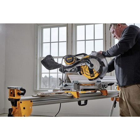 A professional woodworker using a DEWALT sliding miter saw equipped with a 12-inch carbide blade to make a precise crosscut through white crown molding in a residential setting.