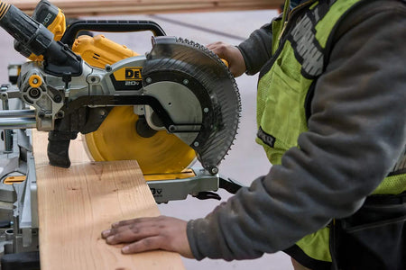 Action shot of the DEWALT 12-inch 40-tooth general purpose blade installed on a cordless miter saw, demonstrating high-performance cutting through a thick dimensional pine board.