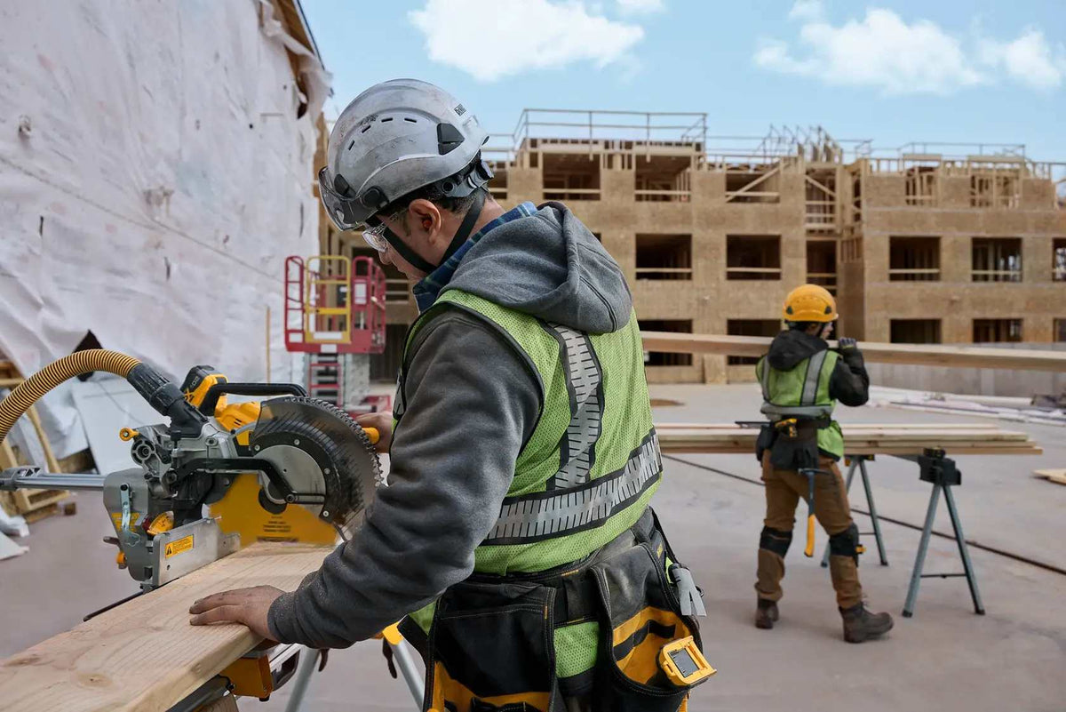 A contractor on a commercial construction site using a DEWALT 12-inch miter saw blade to perform rapid repetitive cuts on framing lumber for a new apartment building project.