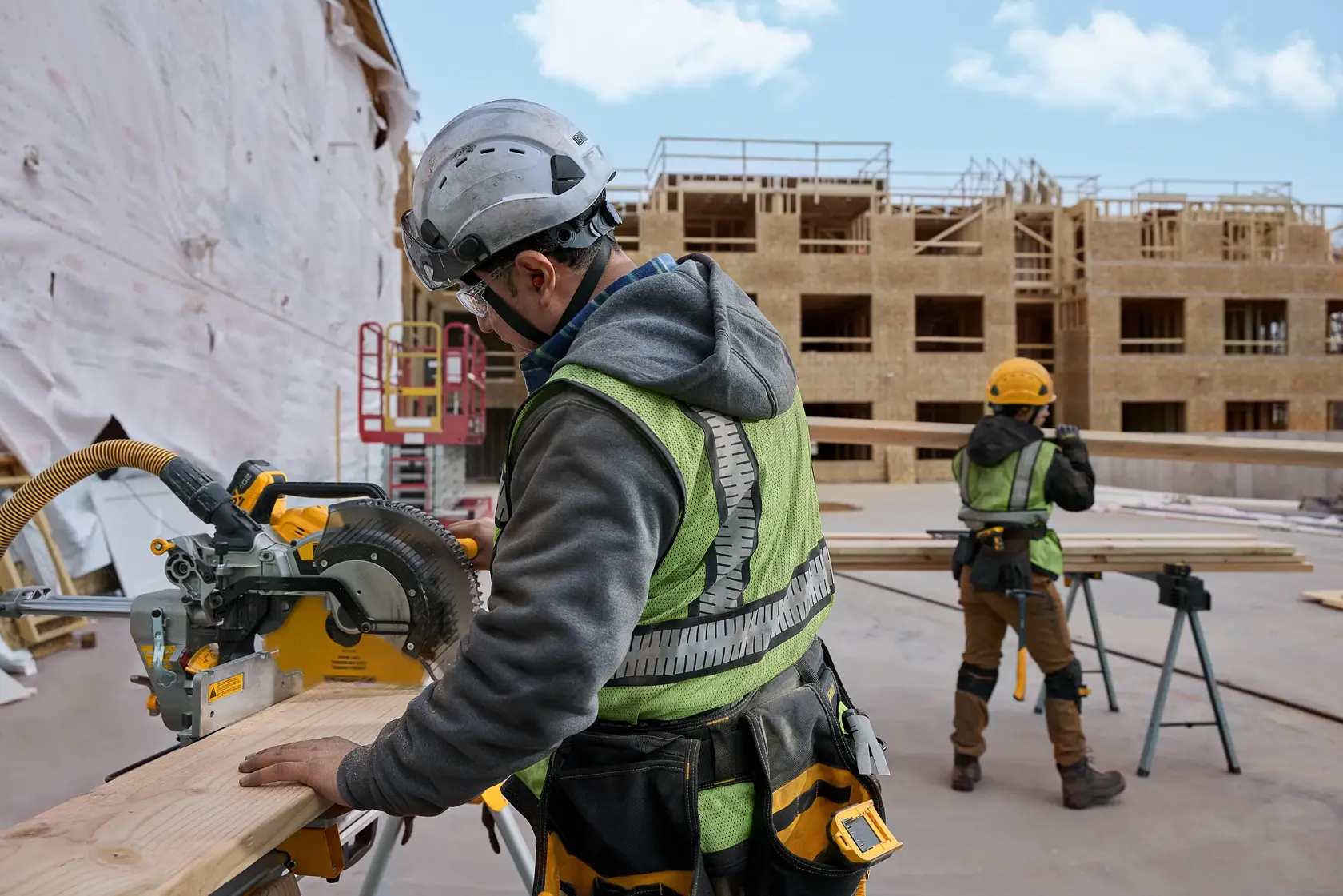 A contractor on a commercial construction site using a DEWALT 12-inch miter saw blade to perform rapid repetitive cuts on framing lumber for a new apartment building project.
