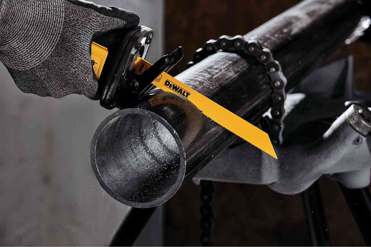 An action photograph showcasing a DEWALT 8 inch 14 TPI reciprocating saw blade cutting through a large industrial steel pipe. The pipe is secured in a chain vise on a jobsite stand, demonstrating the blade's aggressive cutting speed and durability in structural demolition tasks.