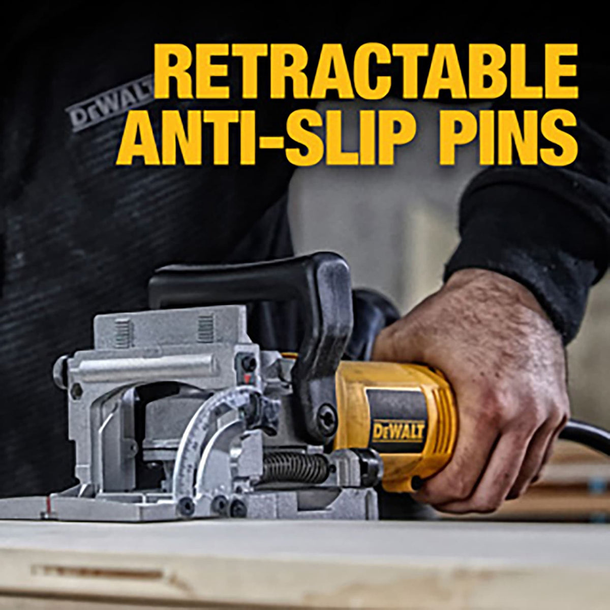 Close-up of the DEWALT DW682K electric plate joiner resting on a wooden board, with a text overlay highlighting the retractable anti-slip pins that hold the power tool securely in place during use.
