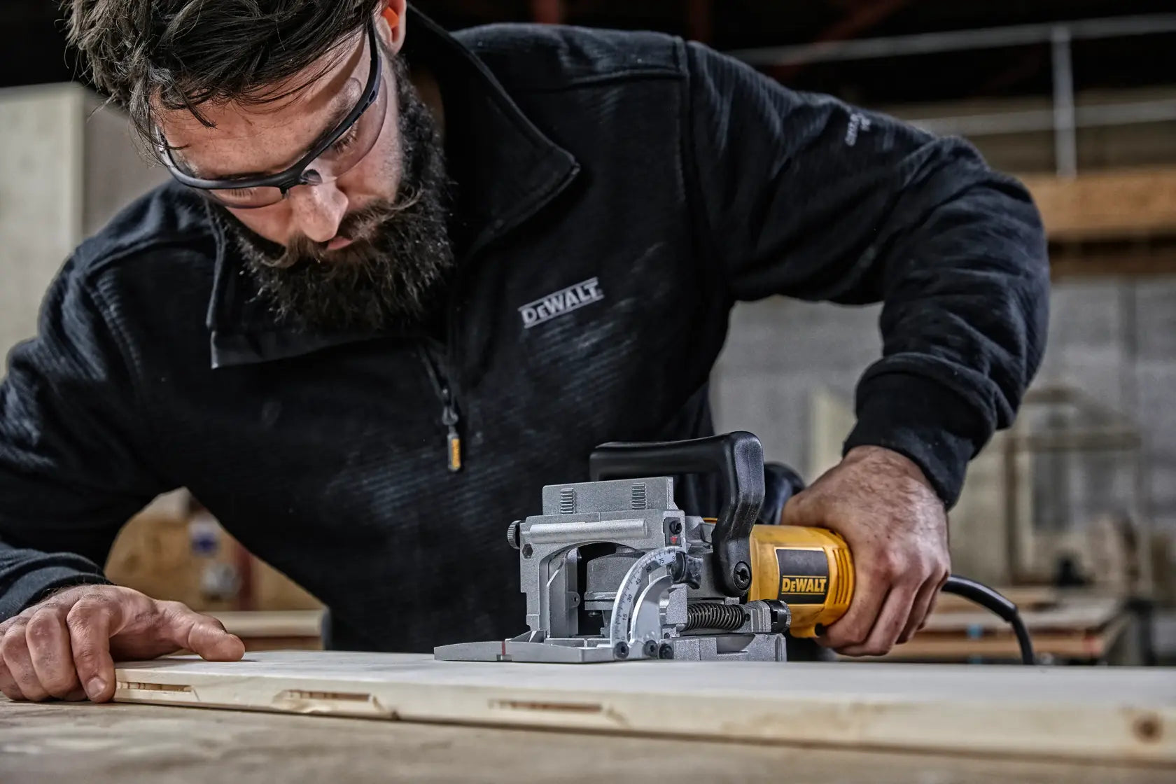 Carpenter utilizing the DEWALT DW682K heavy-duty woodworking biscuit joiner power tool to plunge a precise slot into the edge of a wooden board.