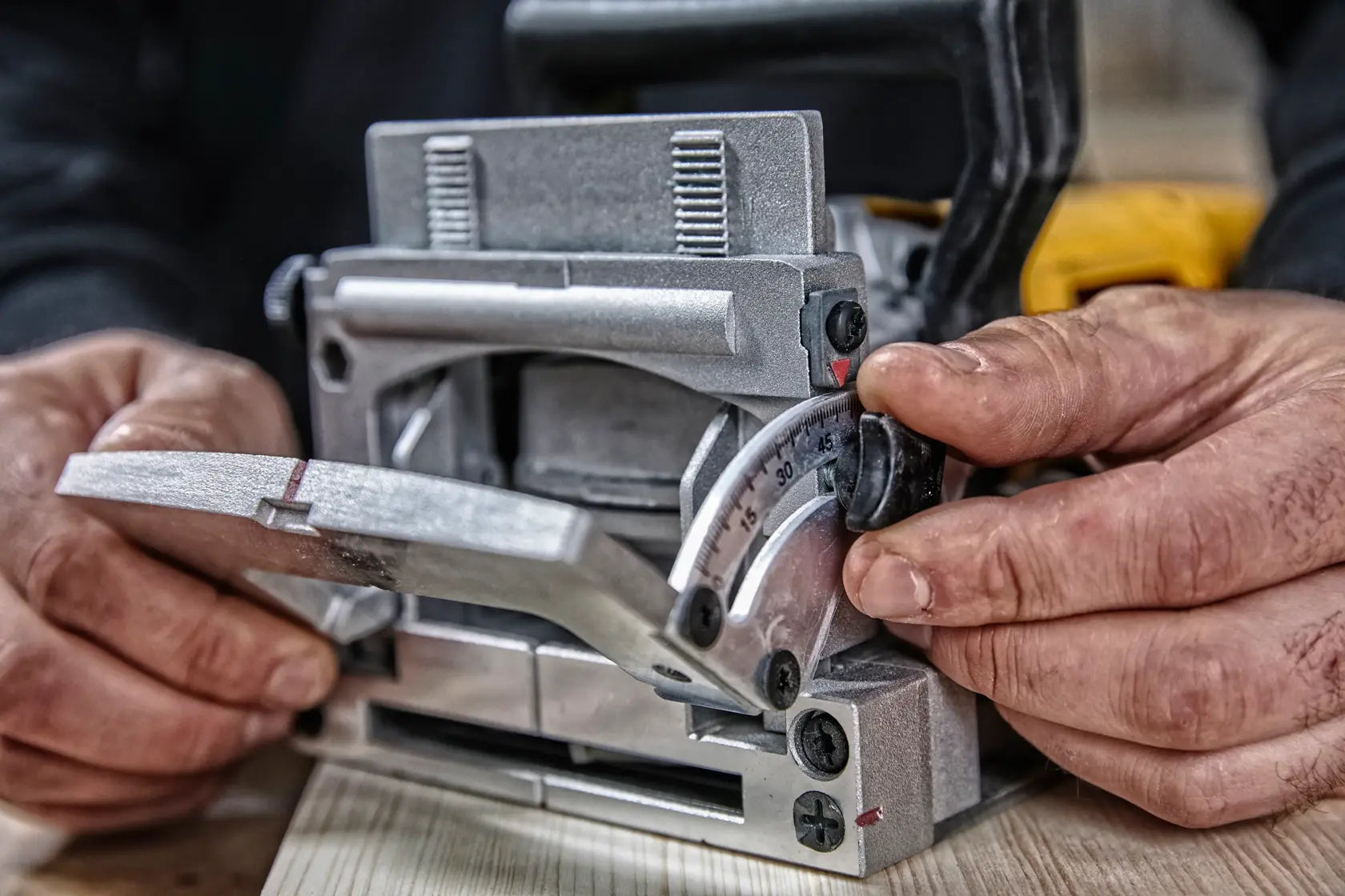 Close-up of a woodworker adjusting the integral one-piece adjustable fence on the DEWALT DW682K biscuit joiner to set a custom angle for accurate carpentry joints.