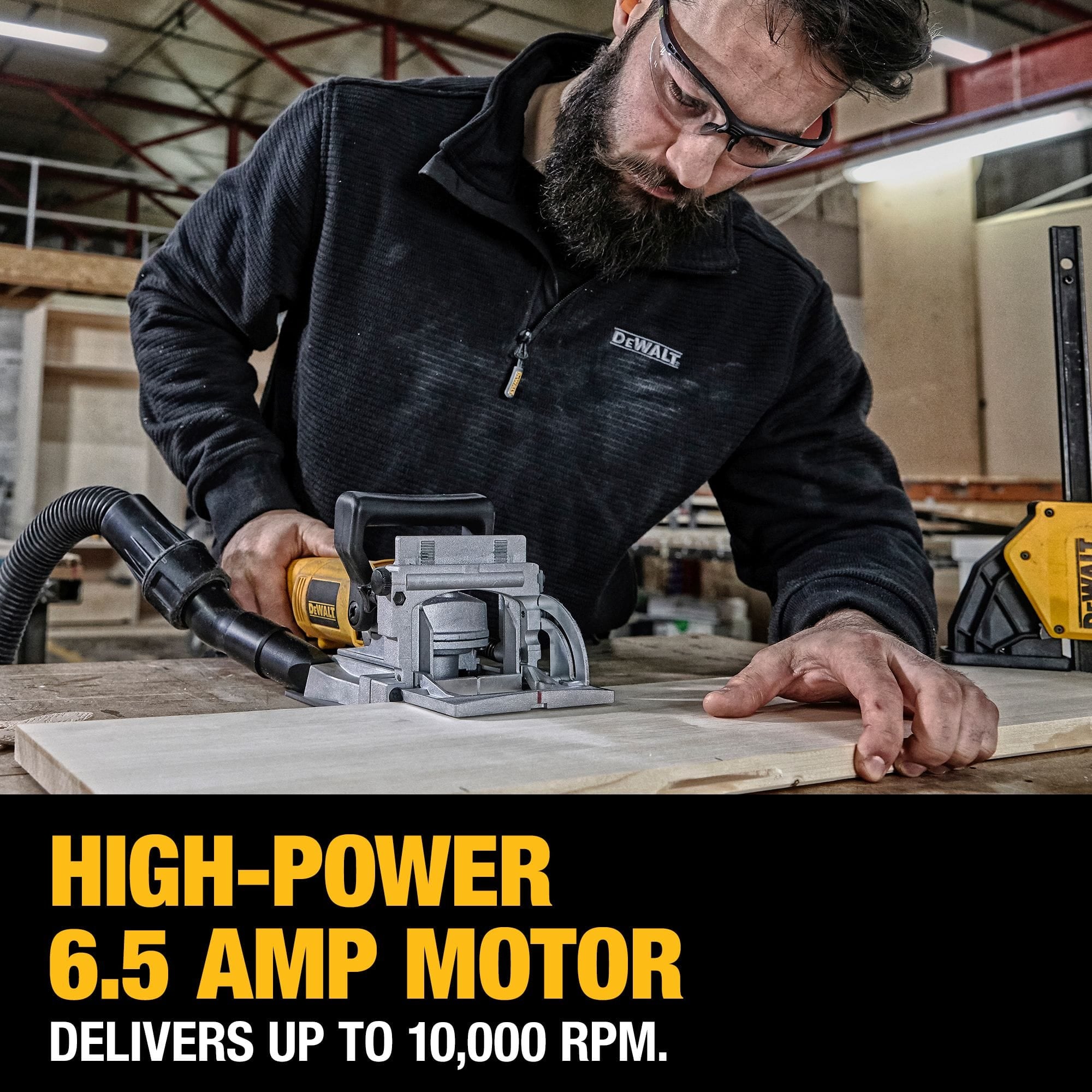 Carpenter operating the DEWALT 6.5 Amp corded electric biscuit joiner with an attached dust extractor, featuring an overlay noting the high-power motor that delivers up to 10,000 RPM.