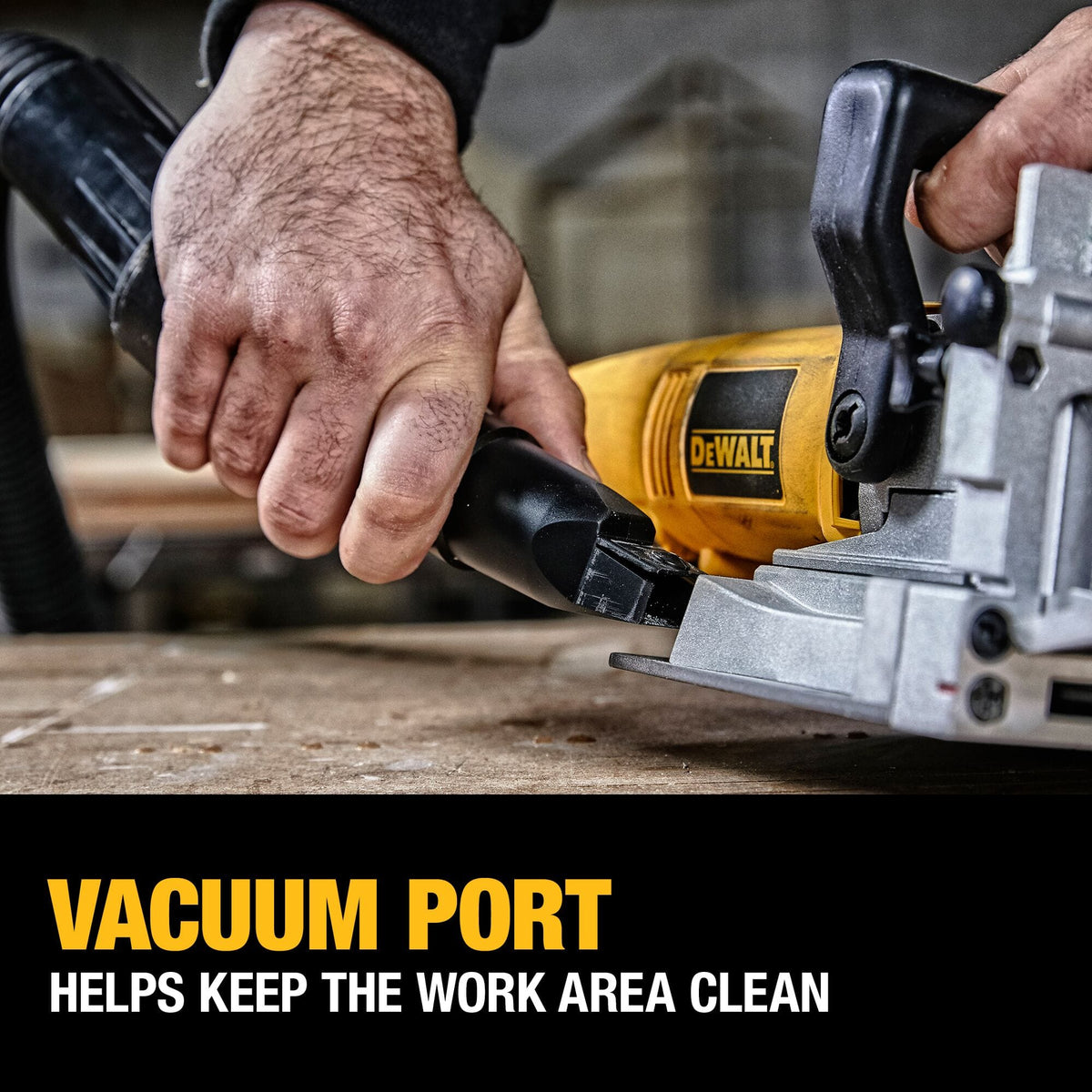 Close-up action shot of a woodworker attaching a dust extraction hose to the vacuum port on the DEWALT DW682K biscuit joiner to help keep the carpentry work area clean.