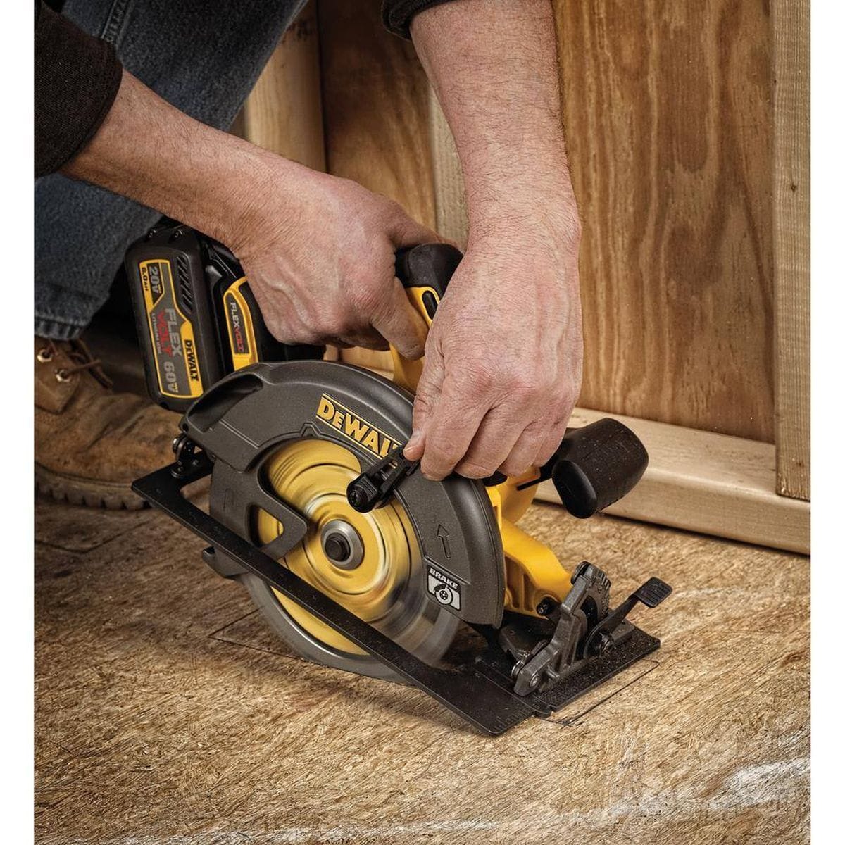 A high-angle action detail shot of the DEWALT FLEXVOLT saw blade performing a plunge cut into a wooden subfloor. The image highlights the aggressive carbide teeth and the stability of the blade body as it navigates a tight, professional-grade cut in a residential workspace.