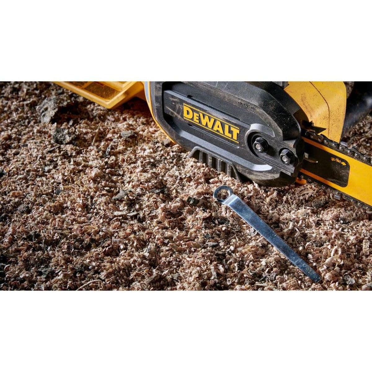 Action detail showing the DEWALT DWCS600 bar retention area and the included multi-tool used for adjusting chain tension amidst heavy wood shavings and jobsite debris.