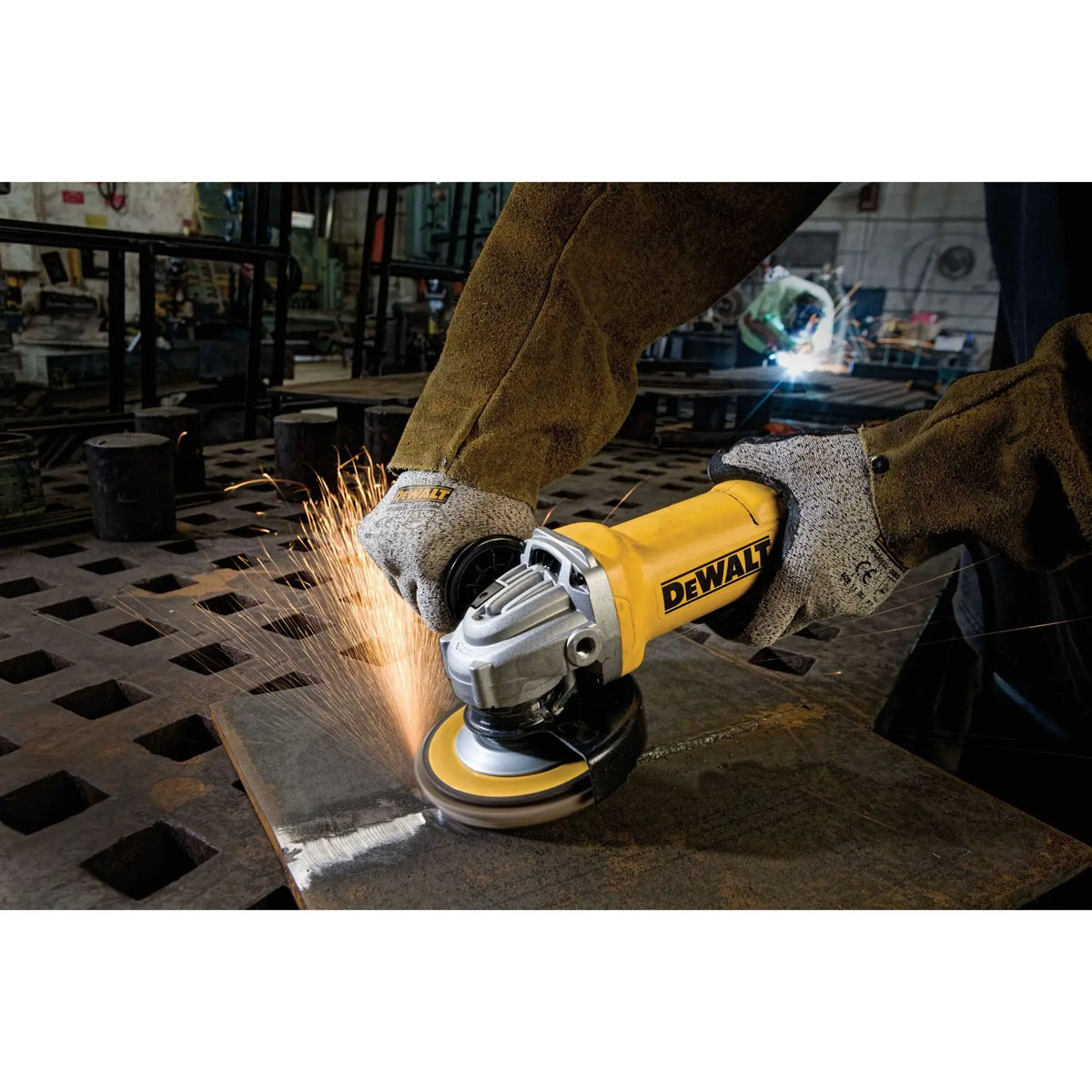 A wide action shot of a professional welder using the DEWALT DWE402 grinder on a heavy steel plate. A stream of sparks demonstrates the aggressive material removal rate of the 11-Amp motor in a fabrication shop environment.
