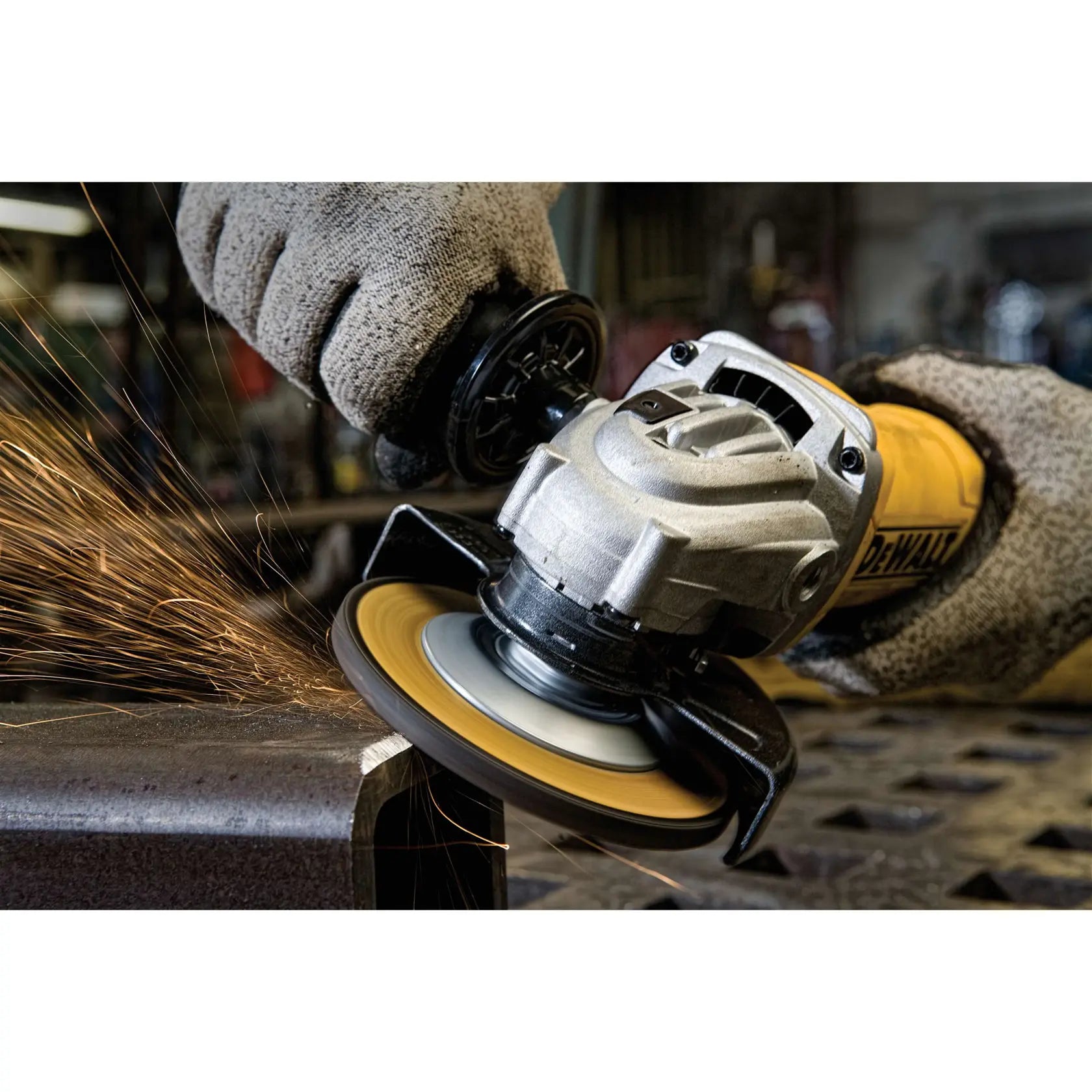 A close-up action photograph of the DEWALT 4.5-inch angle grinder cutting into a structural steel beam. The image captures the high-speed rotation of the abrasive disc and the precise control provided by the ergonomic side handle and paddle switch.
