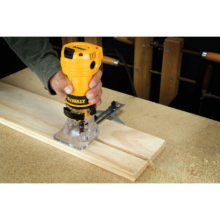 A woodworker using the DEWALT DWE6000 1/4 Inch Laminate Trimmer with the included straight edge guide to rout a precise groove into a wooden board, demonstrating stable single-handed control.