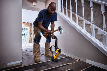 A tradesperson using the DEWALT 2-in-1 flooring tool and mallet to secure engineered wood flooring near a staircase, illustrating the tool's maneuverability and professional results in residential construction.
