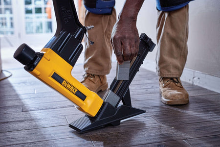 Close-up action shot of an installer loading a strip of 15.5-gauge flooring staples into the DEWALT DWFP12569 magazine while working on a residential hardwood floor renovation.
