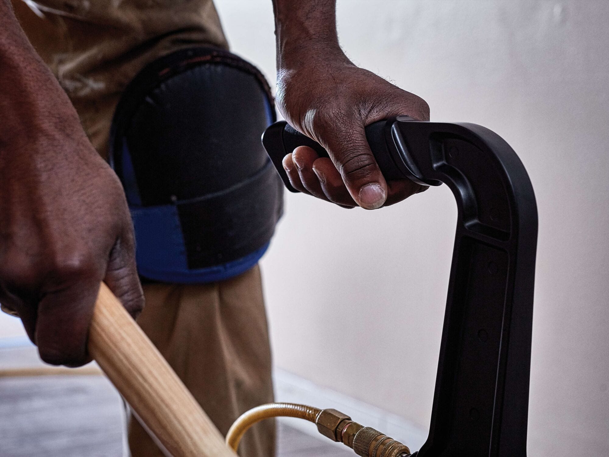 Detailed view of a professional's hand gripping the ergonomic handle of the DEWALT pneumatic flooring tool, showing the air hose connection and the steady control required for high-volume floor fastening.