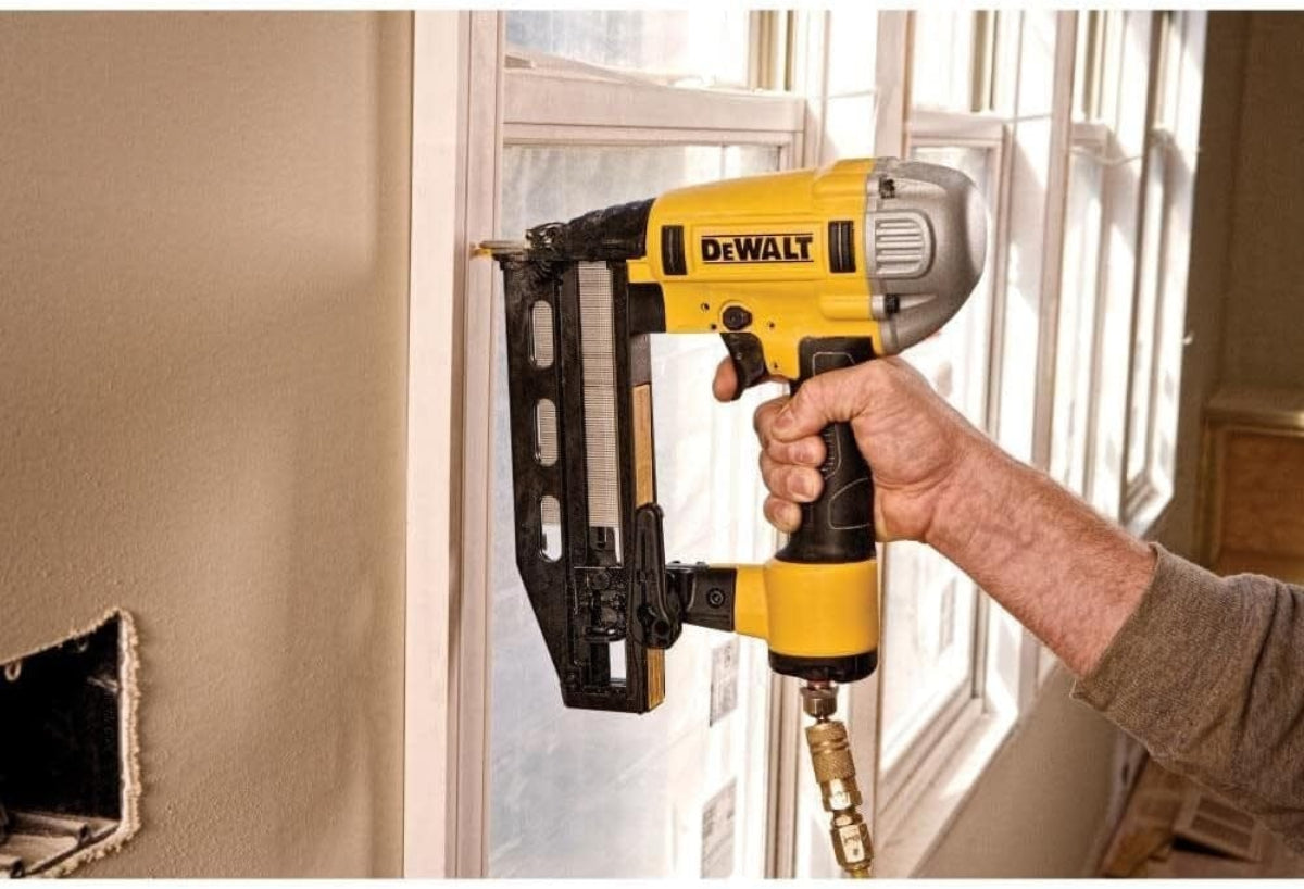 Person using the DEWALT DWFP71917 16‑gauge finish nailer to secure a window frame, demonstrating the tool’s Precision Point accuracy, straight magazine loading, and no‑mar tip performance during detailed interior finish work
