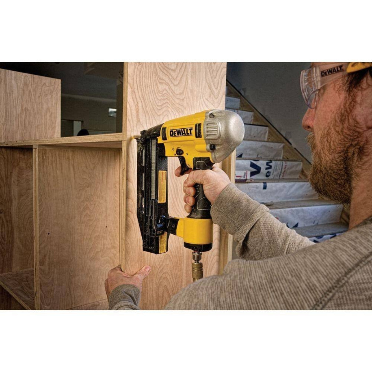 Worker using the DEWALT DWFP71917 Precision Point 16‑gauge finish nailer to attach a wooden panel, highlighting the tool’s accurate nose design, straight magazine, and consistent pneumatic power for cabinetry and fine woodworking tasks