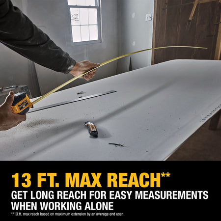 A person using the DEWALT ATOMIC Compact Series 16' Tape Measure on a construction site, demonstrating the 13-foot maximum reach capability for unassisted long-distance measurements.