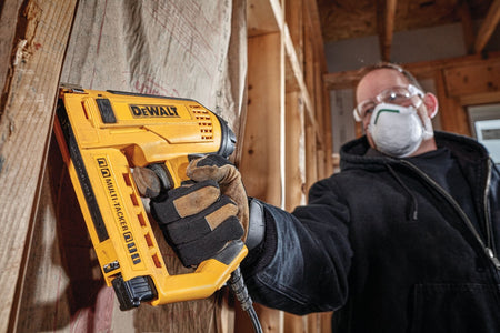 A professional tradesman wearing safety glasses and a dust mask operates the DEWALT DWHT75021 Electric Stapler/Nailer on a construction site, highlighting its versatility for various framing and finishing substrates.