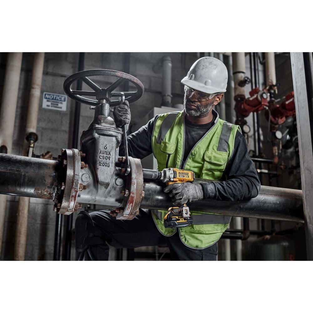 Industrial worker in safety gear using a cordless impact wrench fitted with a DEWALT 1/2-inch drive metric deep impact socket to tighten bolts on a large pipe valve.