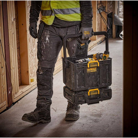 Professional contractor carrying the DEWALT ToughSystem 2.0 light box and integrated storage tote by the large folding handle, demonstrating the modular stacking system's portability while holding cordless power tools on a jobsite.