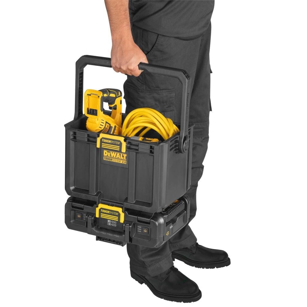 Side view of a worker carrying the stacked DEWALT ToughSystem 2.0 light box and open storage tote, showing the unit loaded with a cordless drill and yellow extension cord for hybrid power operation.