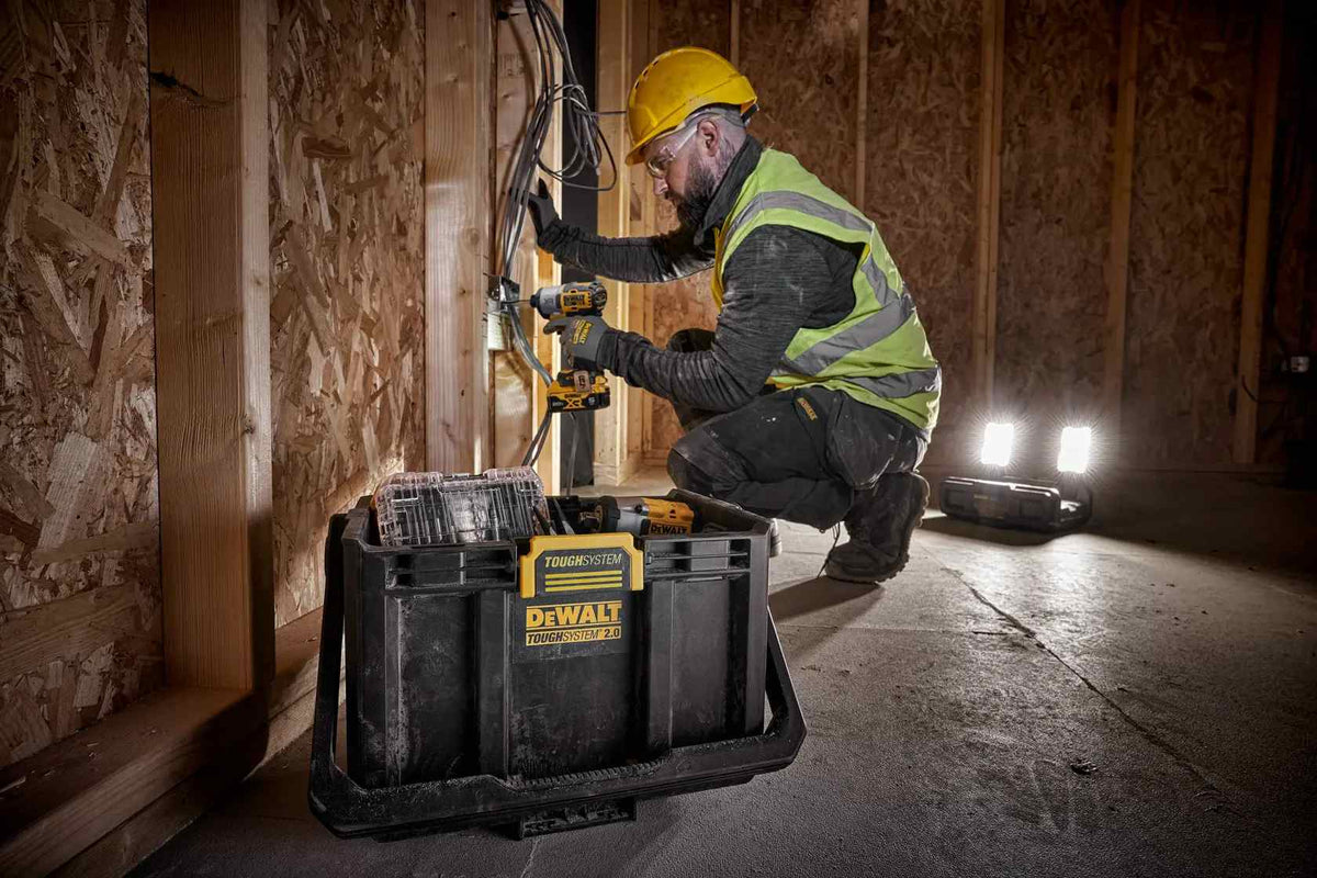 Contractor working on an electrical box with the DEWALT ToughSystem 2.0 light box providing high-intensity illumination from its dual LED heads in a dark construction site.