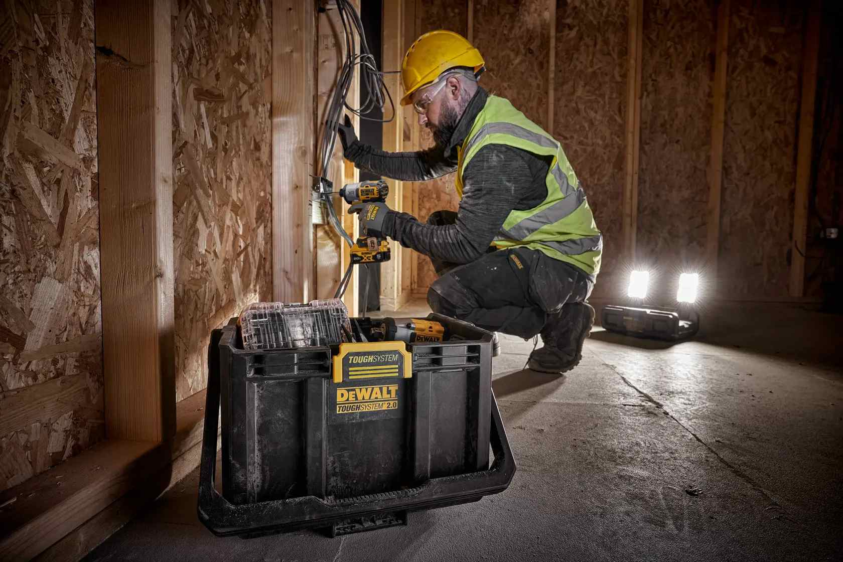 Contractor working on an electrical box with the DEWALT ToughSystem 2.0 light box providing high-intensity illumination from its dual LED heads in a dark construction site.