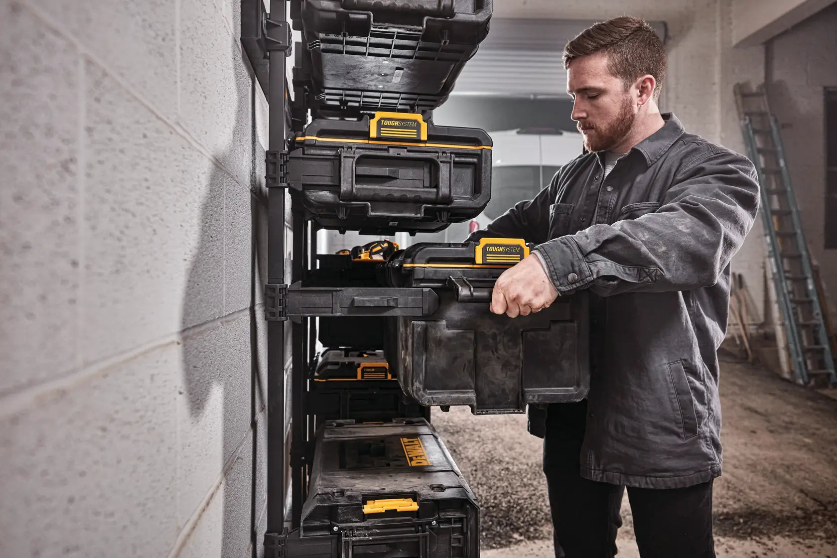 A tradesman sliding the DEWALT DWST08300 large tool box into a wall-mounted TOUGHSYSTEM workshop racking system for professional garage organization.