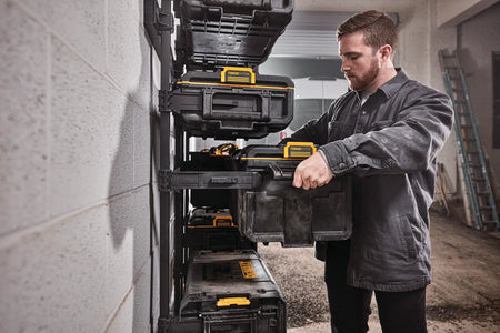 A tradesman sliding the DEWALT DWST08300 large tool box into a wall-mounted TOUGHSYSTEM workshop racking system for professional garage organization.