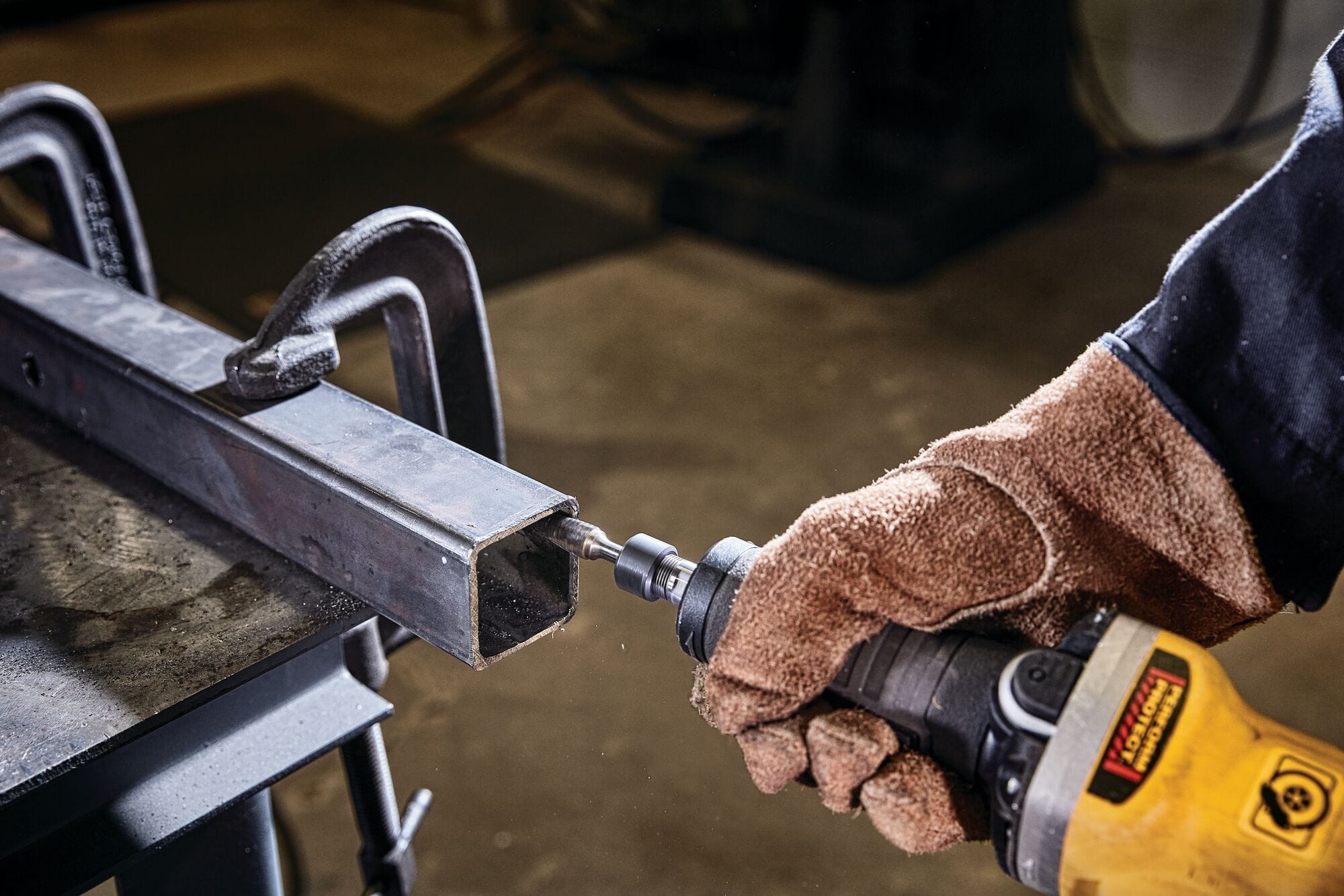 Fabricator using a DEWALT DWE4997VS die grinder to smooth the inner edge of a clamped metal tube, demonstrating controlled deburring and metal finishing with proper safety gear.