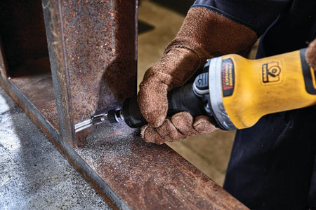 Worker operating a DEWALT DWE4997VS die grinder on a welded steel beam, wearing protective gloves while performing high‑speed grinding and surface preparation in a workshop setting.
