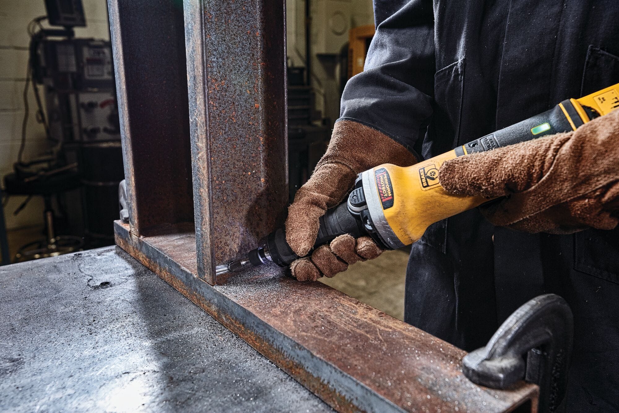Metalworker using a DEWALT DWE4997VS die grinder to smooth the inner corner of a rusted steel beam secured with a clamp, showing controlled grinding and industrial surface preparation.