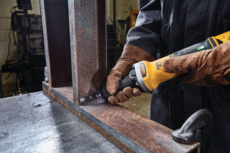 Metalworker using a DEWALT DWE4997VS die grinder to smooth the inner corner of a rusted steel beam secured with a clamp, showing controlled grinding and industrial surface preparation.