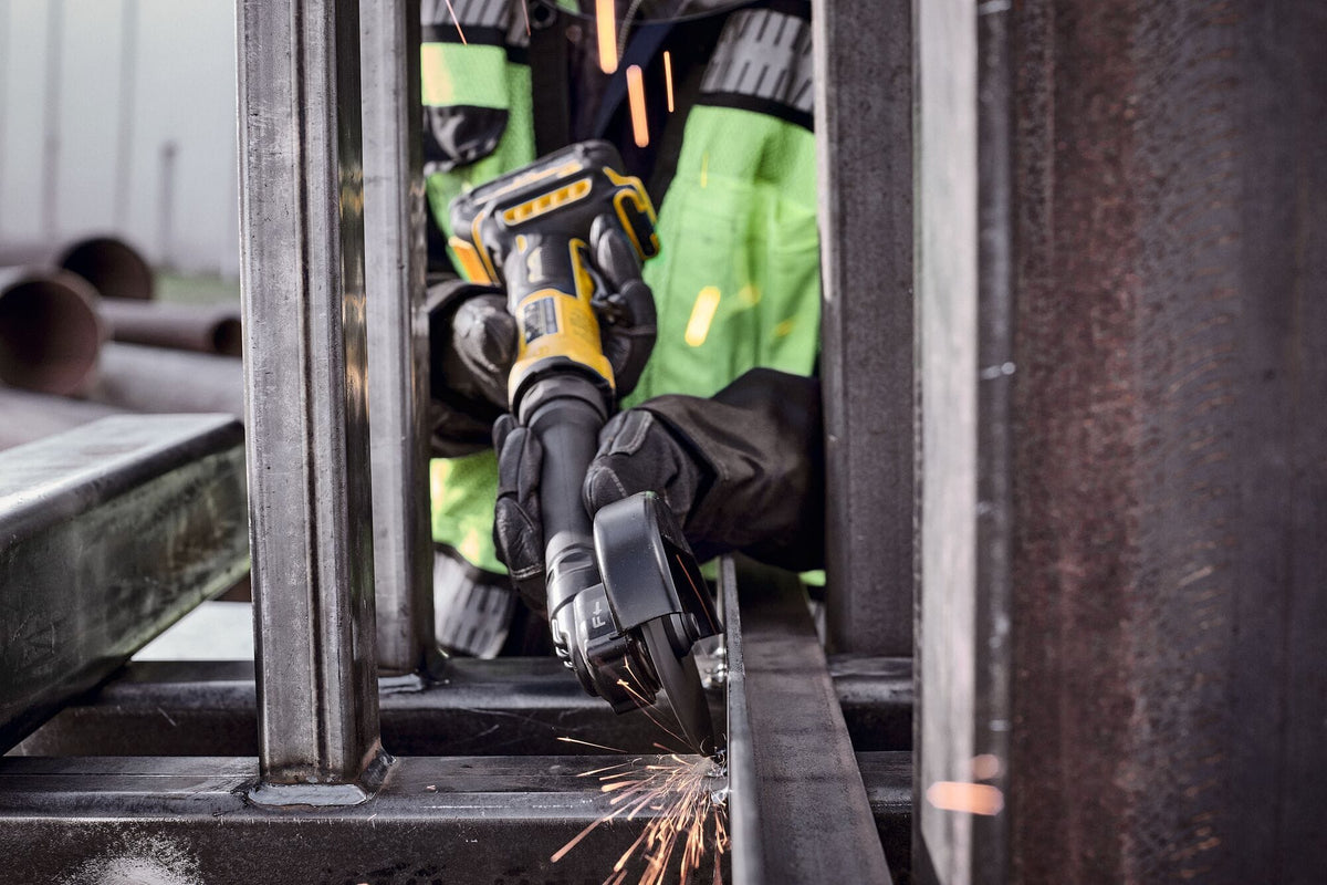 Construction worker utilizing the extended reach of the DEWALT 4 inch cordless metalworking tool to cut a vertical steel beam in a confined space, highlighting the maneuverability of the DCG432XGE2.