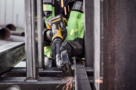 Construction worker utilizing the extended reach of the DEWALT 4 inch cordless metalworking tool to cut a vertical steel beam in a confined space, highlighting the maneuverability of the DCG432XGE2.
