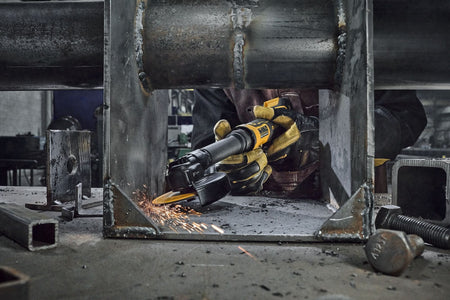 Fabricator operating the DEWALT ATOMIC 20V MAX extended cut-off tool to grind inside a restricted steel joint, showing the low profile gearcase engineered for demanding narrow space cutting applications.