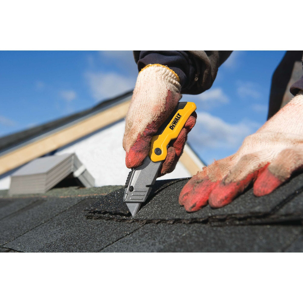 Close up shot of a professional roofer using the DEWALT folding retractable utility knife to precisely cut asphalt shingles during a roof installation.