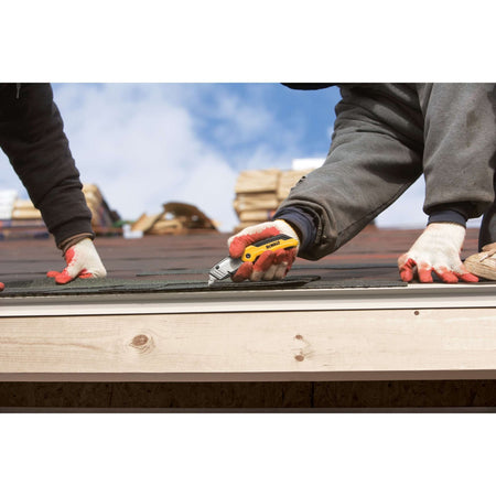 Action shot of a worker using the DEWALT metal body utility knife to trim roofing material along a drip edge, demonstrating the tool's control and ergonomic grip.