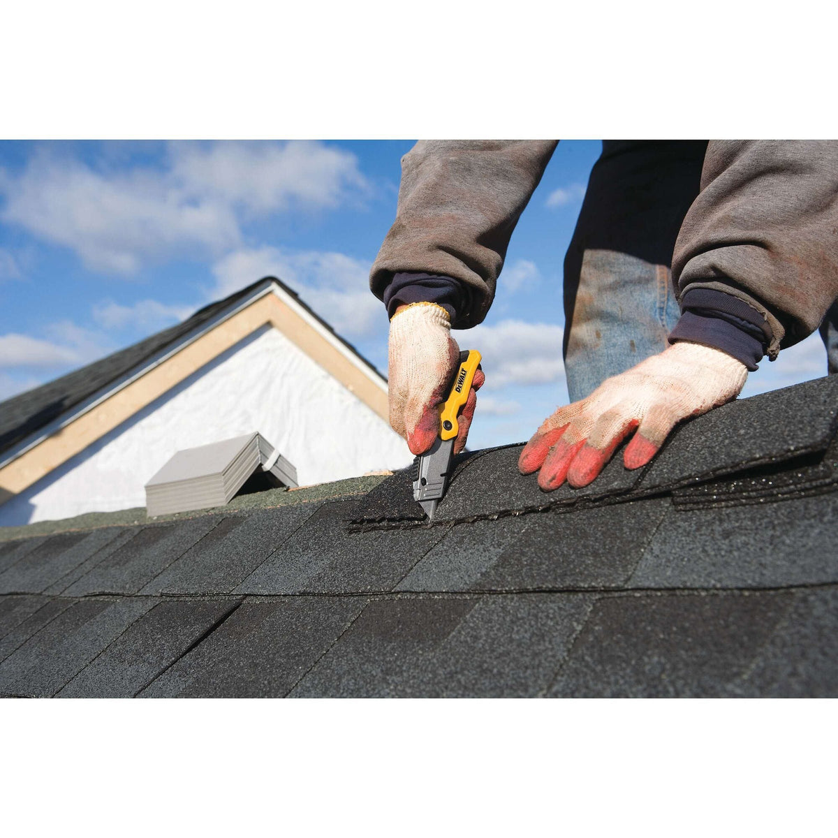 Wide view of a contractor on a residential roof using the DEWALT DWHT10035L folding knife to score shingles, showcasing the tool's portability for outdoor construction projects.