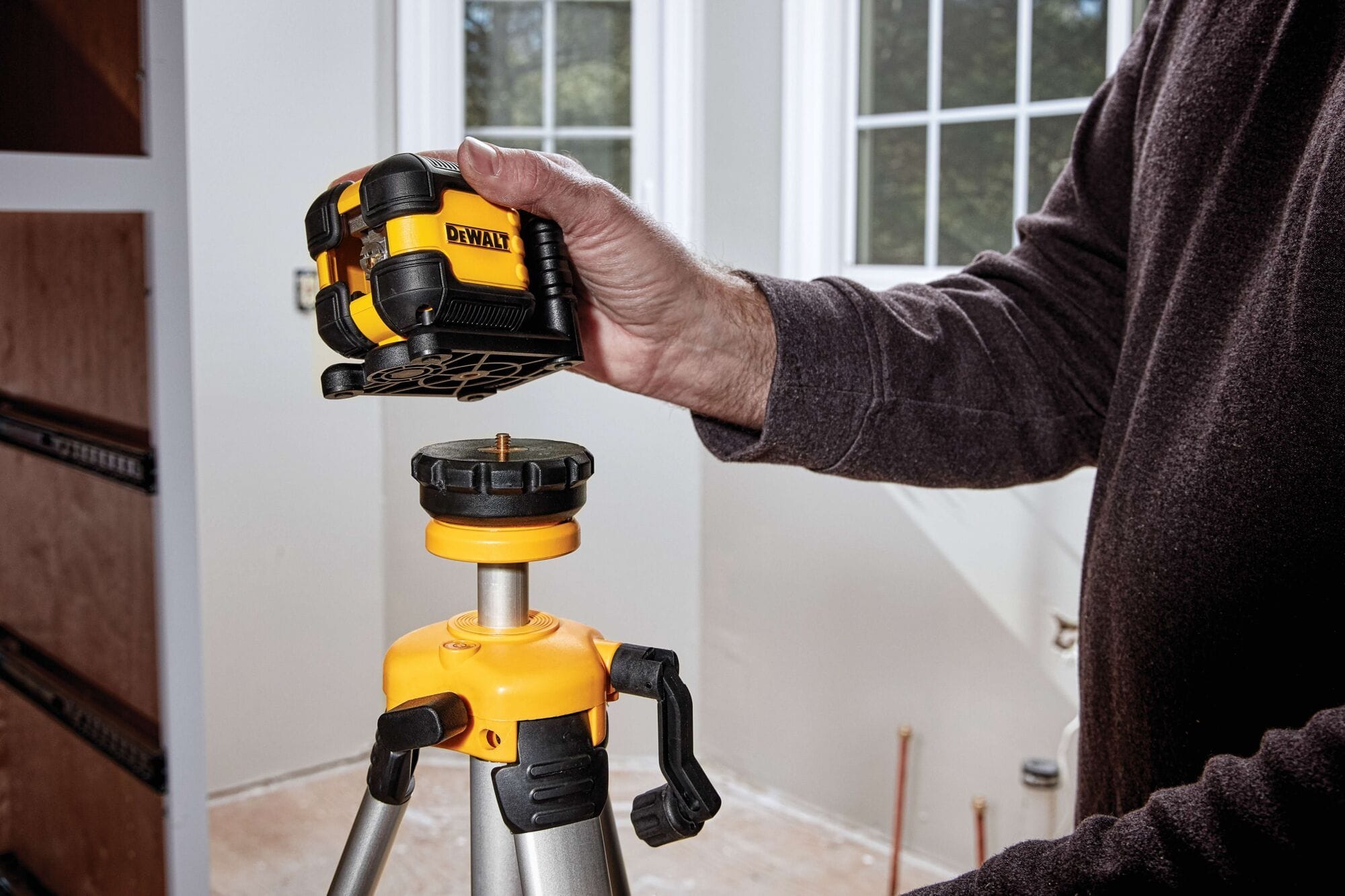 A contractor attaching the DEWALT DW08802CG green laser level to a tripod using the 1/4 inch threaded mount during an indoor construction and leveling project.