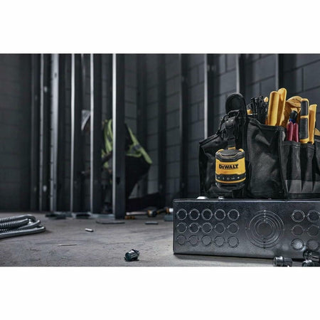 The DEWALT mini Bluetooth speaker hangs by its strap from a professional tool pouch on an electrical jobsite with metal studs in the background.