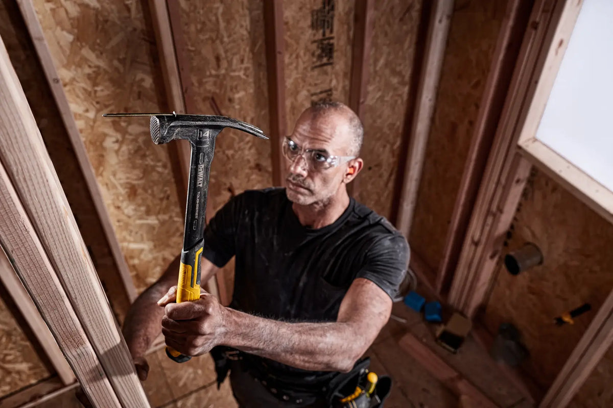 Action shot showing a professional contractor utilizing the integrated magnetic nail starter on the DEWALT TOUGHSERIES hammer for easy one-handed nail placement.