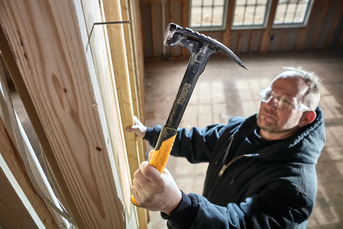 Close up of a carpenter using the DEWALT DWHT51138X hammer to drive a nail into a wood stud during a residential framing project, showcasing the impact power of the milled face.
