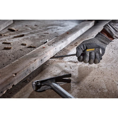 Close-up of a worker using a DEWALT demolition screwdriver to pry a wooden board on a concrete floor, illustrating the heavy-impact durability and bend resistance of the S2 steel bar.