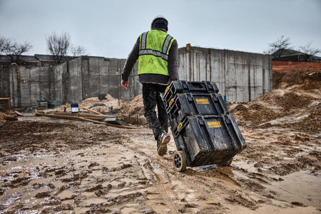 Worker pulling stacked DEWALT ToughSystem tool boxes across wet muddy construction site demonstrating weather resistant durability and mobile tool transport in harsh jobsite conditions.