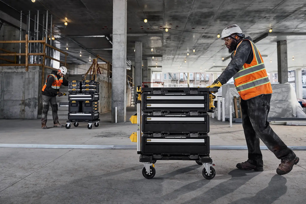 A wide lifestyle shot of a contractor pushing a large DEWALT ToughSystem 2.0 rolling tower across a concrete floor. The DWST08050 charger box is securely stacked within the modular system, showcasing the mobile efficiency of the centralized charging station.