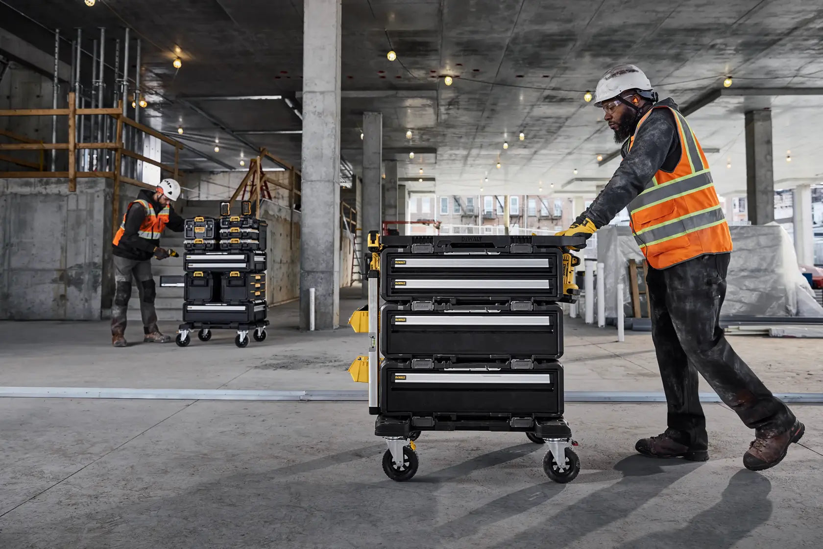 A wide lifestyle shot of a contractor pushing a large DEWALT ToughSystem 2.0 rolling tower across a concrete floor. The DWST08050 charger box is securely stacked within the modular system, showcasing the mobile efficiency of the centralized charging station.